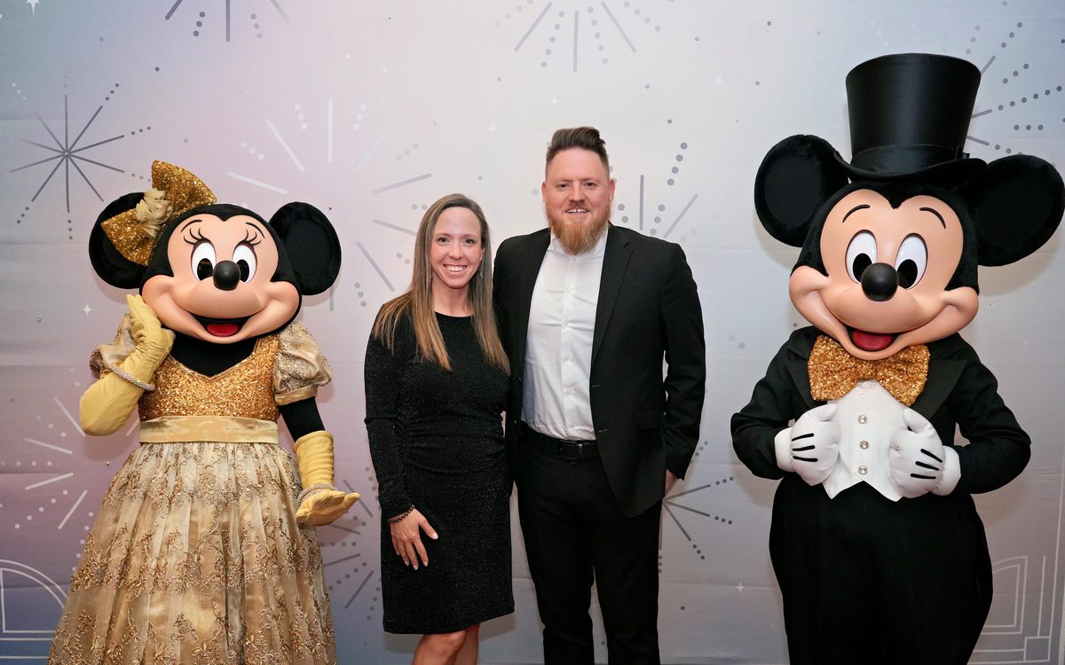 Lynne and her husband in formalwear with Mickey and Minnie Mouse
